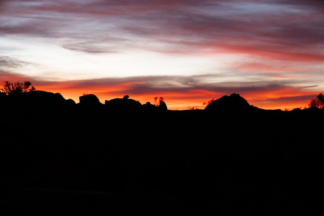Orange sunset clouds above a dark desert skyline.